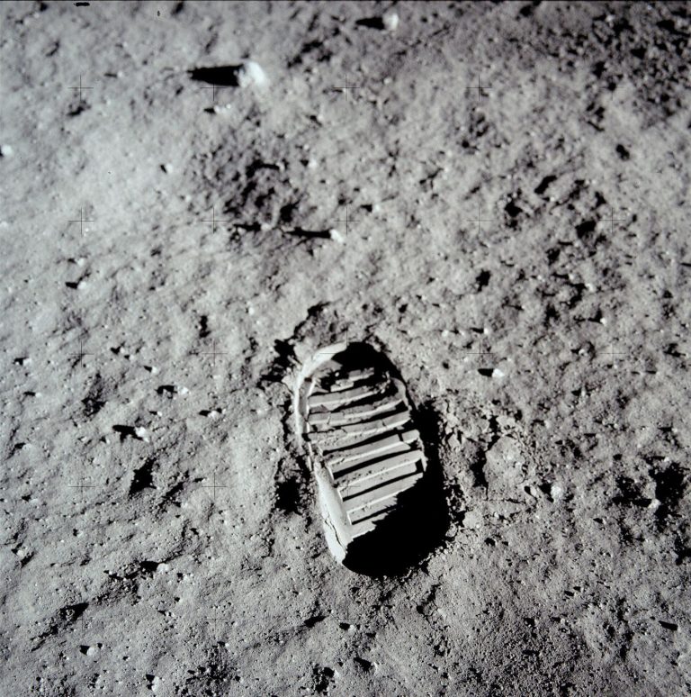 A detailed view of the moon surface showing a rugged lunar landscape pockmarked with craters under stark sunlight.